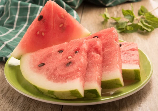 Sliced watermelon arranged in a green plate on a black background.