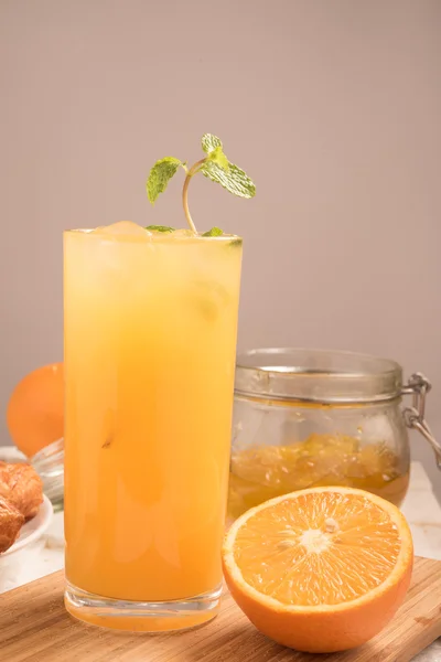 Fresh orange juice in a glass on a wooden panel with jam and half orange