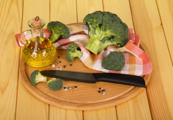 Sliced broccoli, oil in the decanter and spices for cooking on background of light wood