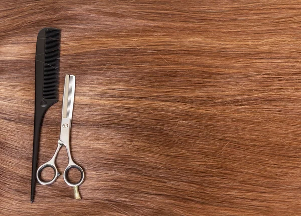 Comb and barber scissors on  background of beautiful brown hair.