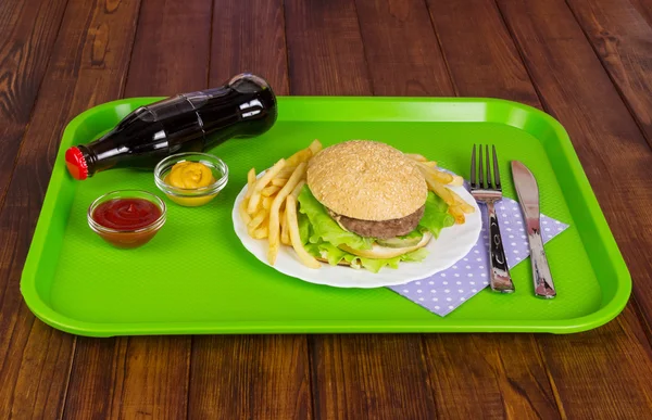 Hamburger, french fries, sauces and cola bottle in  dark wood.