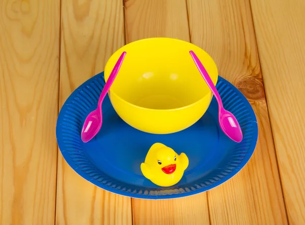 Colored plastic ware and rubber duck on  background  light wood.