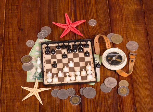 Accessories for  traveler: chess, compass and money on  dark wood.