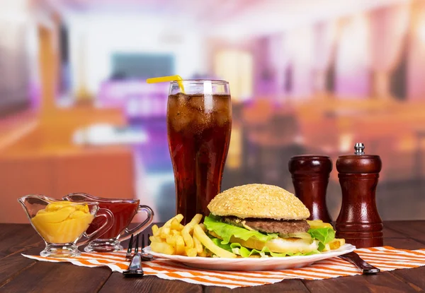Hamburger, french fries, glass cola, sauces and spices  in  cafe.