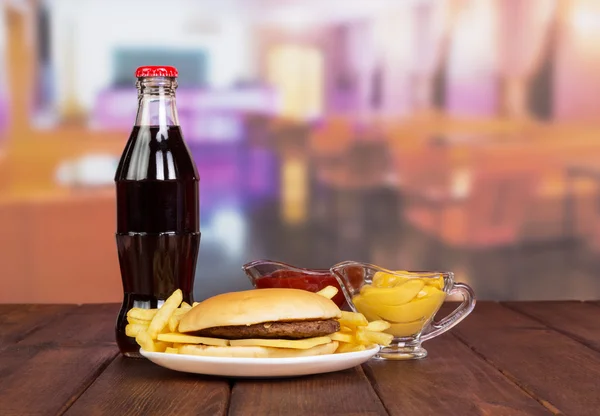 Fast set: hamburger, fries, bottle  cola, sauces on  background cafe.