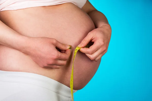 Pregnant woman with centimeter on blue background.