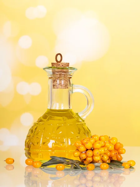 Bottle sea buckthorn oil and berries on abstract yellow background.