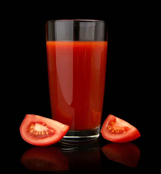 Glass of tomato juice with quarters of tomatoes on black