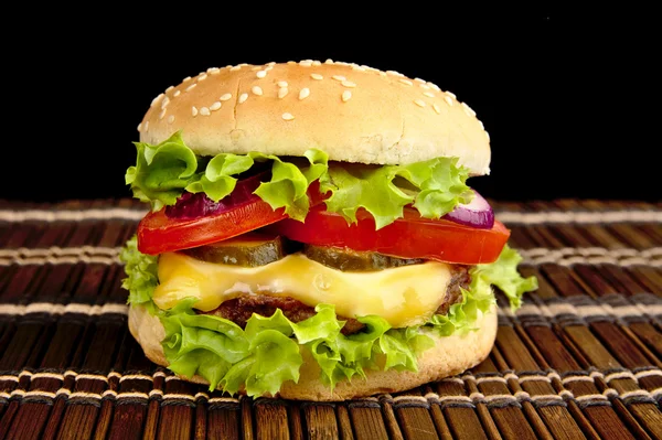 Big single cheeseburger on wooden mat on black background