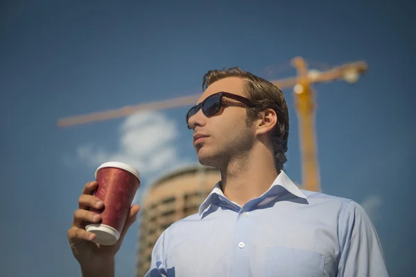 Young businessman drinking coffee on a background of construction