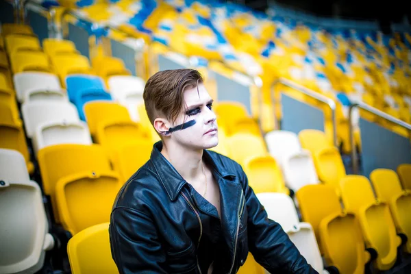 Relaxed fashion for men in leather jacket posing while sitting in the stadium