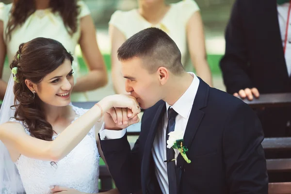 Bride groom kisses hand, sitting on the bench