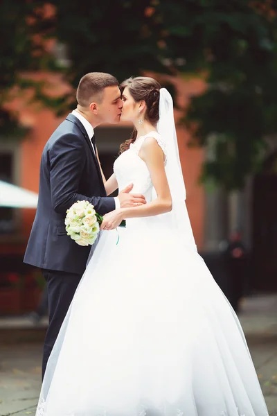 Couple in wedding attire with a bouquet of flowers and greenery is in the hands against the backdrop of the garden at sunset, the bride and groom