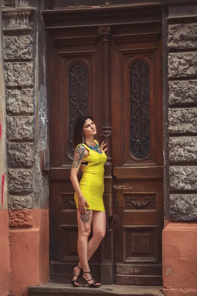 A beautiful woman in a yellow dress, tattoos, leaned on old door