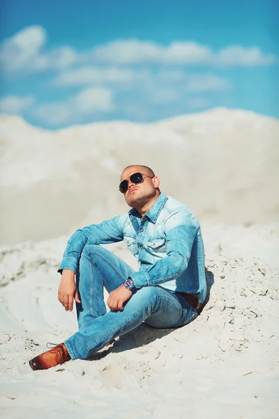 Young man in glasses lies in jeans clothes on the sand in Dubai