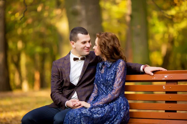 Groom and Bride sitting on bench in a park. smile wedding dress.