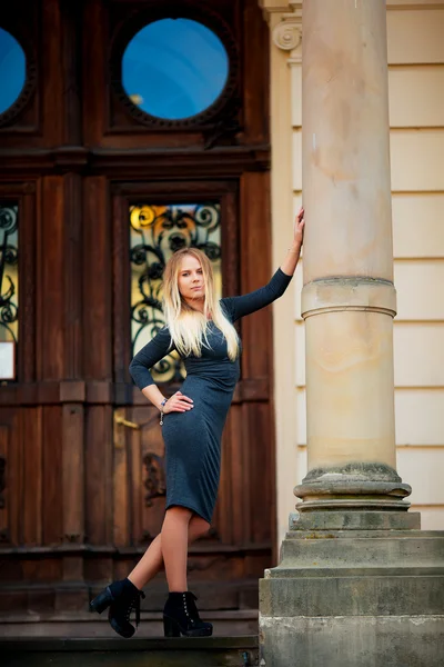 Young girl posing in a  dress for the camera on a background of brown wooden door column with copy space for your text message or content, confident stylish woman looks to the side