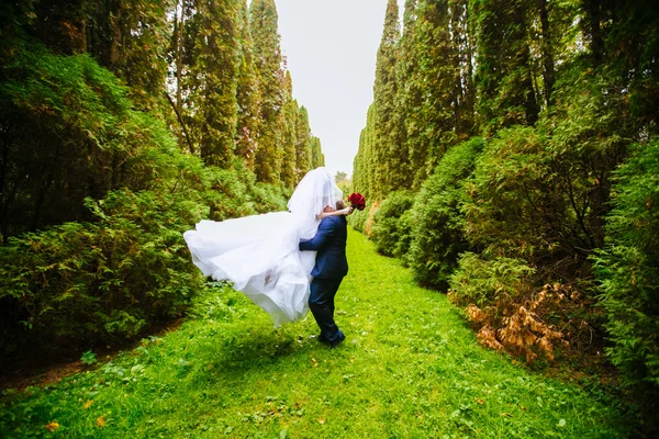 Loving couple having fun in the forest, kissing and whirling around themselves, happy bride and groom enjoying wedding day