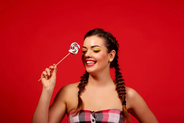 Close Up. Brunette girl with red lips, holding colorful lollipop. The beauty model portrait sweet candies on a red background.