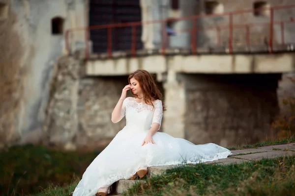 Full length side view of one beautiful sensual young brunette bride in long white wedding dress and veil standing in forest holding bouquet outdoor on natural background, horizontal picture