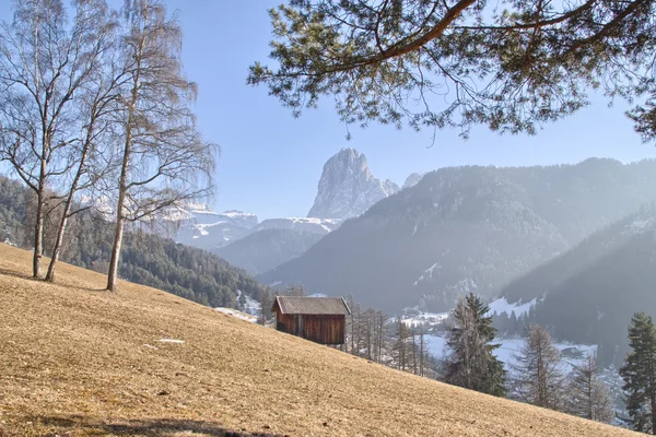 Mountain hut in valley of green forests and snowy peaks in winte