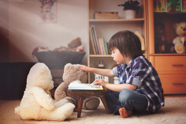 Cute little child, preschool boy, reading a book to his teddy be