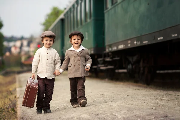 Two boys, dressed in vintage clothing and hat, with suitcase