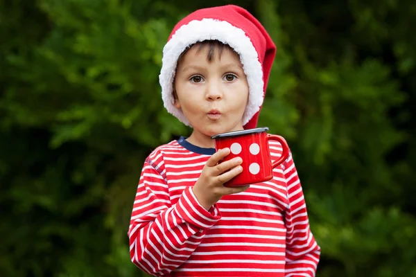 Sweet boy in striped shirt with santa hat, holding cup with tea