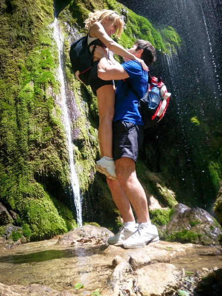 Romantic image, man lifted up woman beside forest waterfall