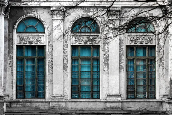 Facade of old abandoned building with three large arched windows of blue glass and columns. Monochrome background