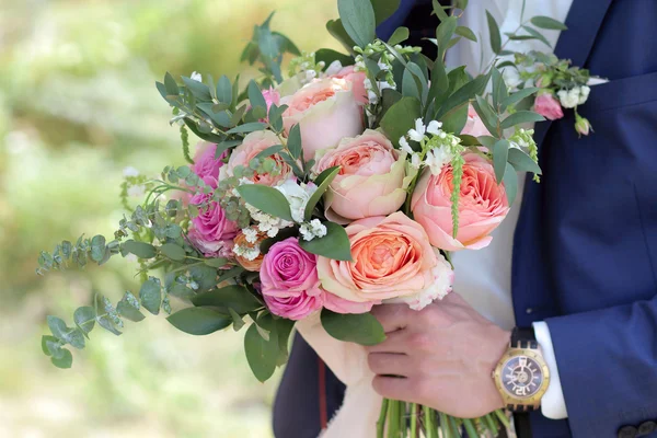 Groom holding a beautiful bridal bouquet. Wedding bouquet of peach roses by David Austin,  single-head pink rose aqua, eucalyptus, ruscus, gypsophila