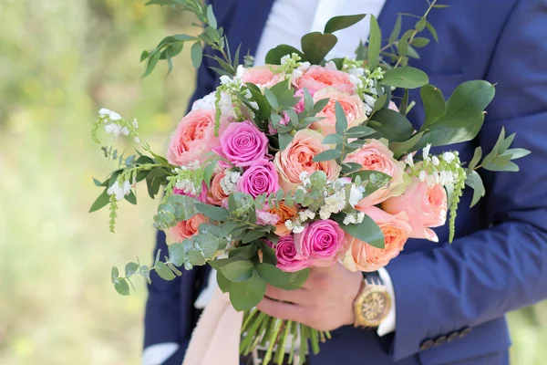 Beautiful bridal bouquet in hands of the groom. Wedding bouquet of peach roses by David Austin,  single-head pink rose aqua, eucalyptus, ruscus, gypsophila