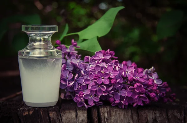 Perfume bottle with a sprig of lilac on a wooden background