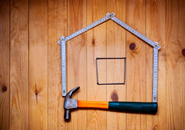 Set of different work tools are in  form of  house: hammer, meter, nails over  wooden background