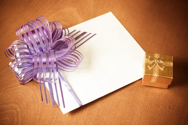 Note Card With Purple Bow And Gold Gift Box On Wooden Background. Vintage style