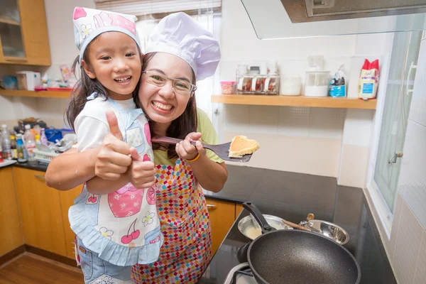 Asian mother and daughter enjoy making pancake in kitchen at home