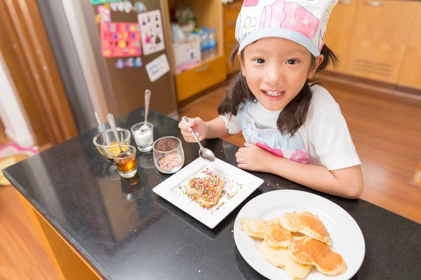 Little Asian girl enjoy decorate pancake with decorate sugar pill in kitchen