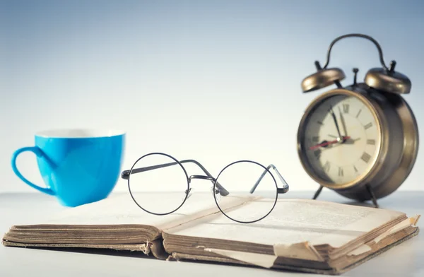 Open book, clock, cup and glasses