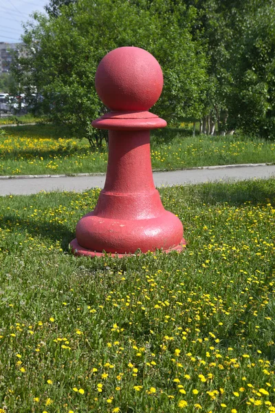 Chess pieces - red pawn on the green grass in the park \