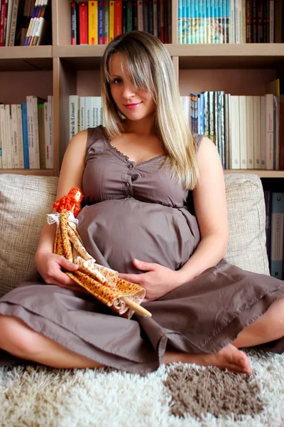A young pregnant woman sitting in a room with soft doll