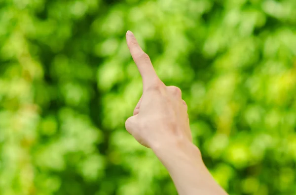 Spring and nature theme: man\'s hand showing gesture on a background of green grass in the spring, first-person view