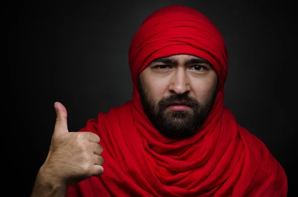 Turkish and Arabic theme: beautiful Arabic man with a beard in a red scarf showing gestures isolated on black background in studio