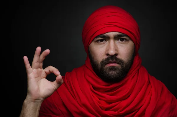 Turkish and Arabic theme: beautiful Arabic man with a beard in a red scarf showing gestures isolated on black background in studio