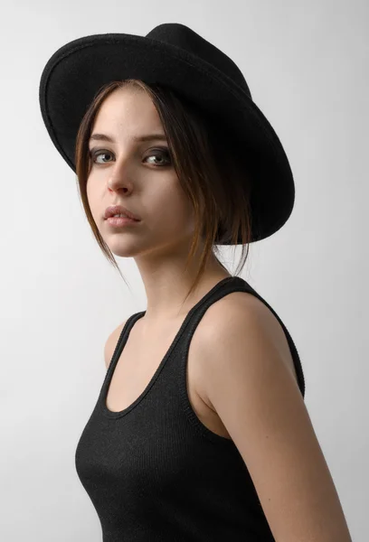 Dramatic portrait of a girl theme: portrait of a beautiful young girl in a black hat and a black shirt isolated on gray background in studio