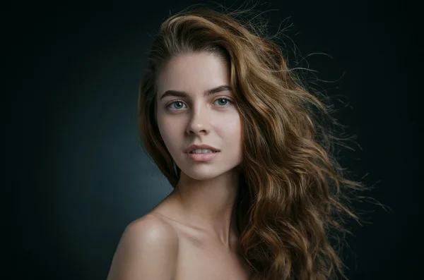 Dramatic portrait of a girl theme: portrait of a beautiful girl with flying hair in the wind against a background in studio