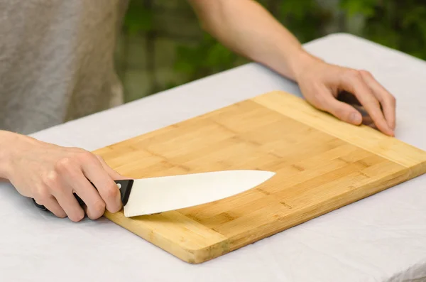 Cooking theme: a man holding a knife next to a wooden cutting board on a background of green grass in summer