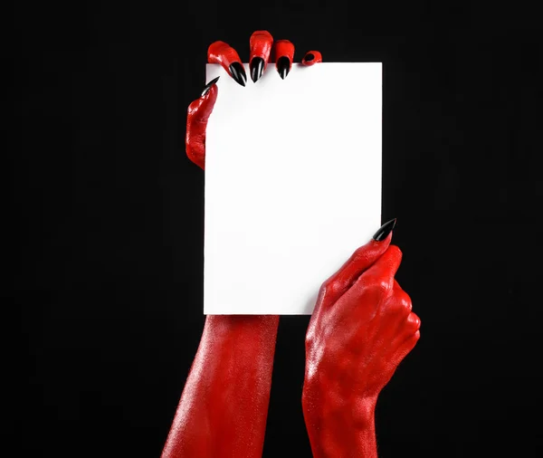 Halloween theme: Red devil hand with black nails holding a blank white card on a black background