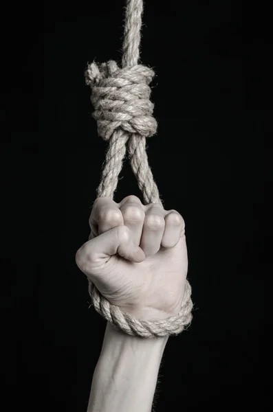 Suicide and depression topic: human hand hanging on rope loop on a black background