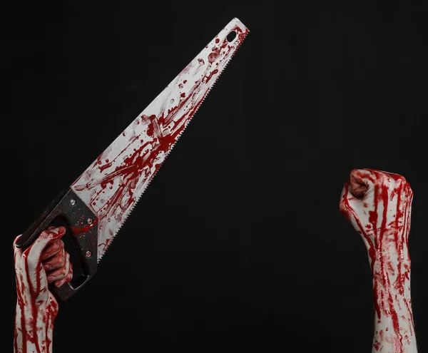 Halloween theme: bloody hand holding a bloody saw on a black background