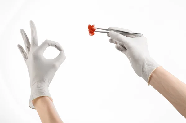 Surgery and Medical theme: doctor\'s hand in a white glove holding a surgical clip with a bloody tampon isolated on a white background in studio